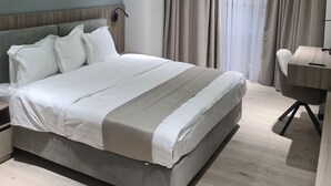 A modern bedroom with a large bed, a desk, and a curved window with curtains. - Asia Grand Hotel (Dushanbe)