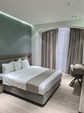 A modern bedroom with a large bed, a desk, and a curved window with curtains. - Asia Grand Hotel (Dushanbe)