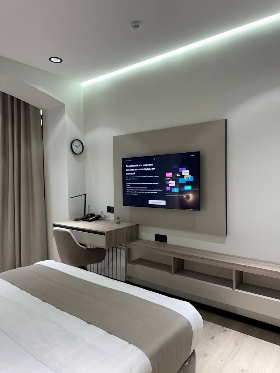 A modern hotel room with a bed, desk, and TV displaying a digital interface.