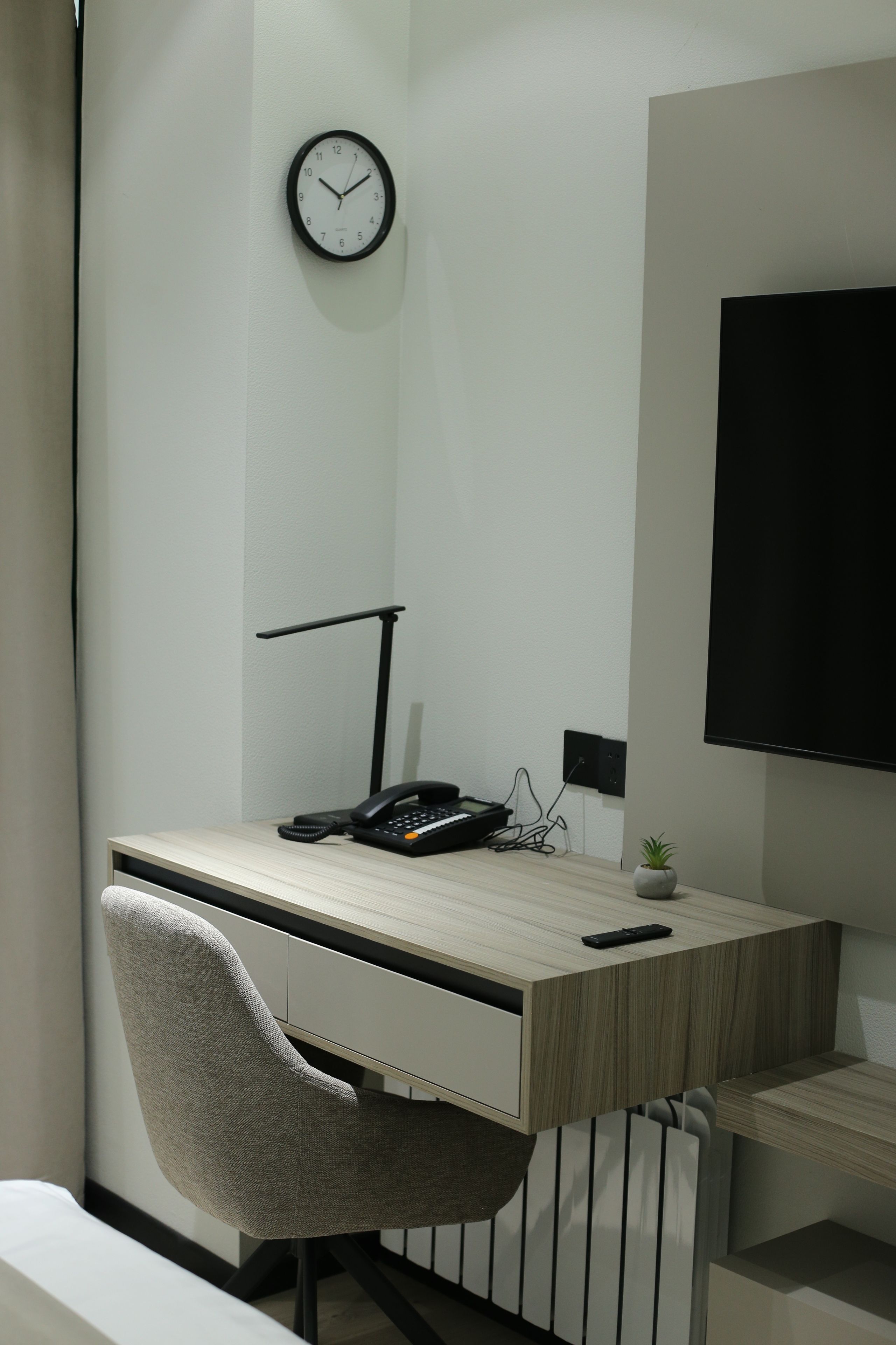 A modern office desk with a chair, a clock, a phone, and a small plant.