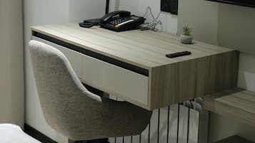 A modern office desk with a chair, a clock, a phone, and a small plant.
