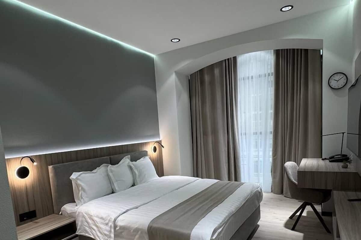 Een moderne slaapkamer met een groot bed, nachtkastjes, een bureau en een gebogen raam met gordijnen.