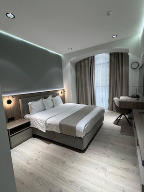 A modern bedroom with a large bed, bedside tables, a desk, and a curved window with curtains. - Asia Grand Hotel (Dushanbe)
