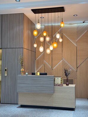 Un mostrador de recepción de diseño moderno, con un patrón geométrico en la pared y una serie de lámparas esféricas colgantes.