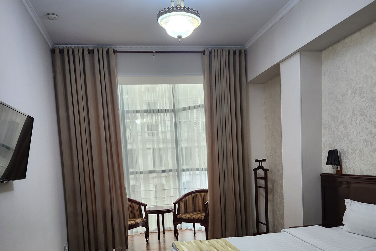 A hotel room with a bed, a desk, a chair, a TV, and a window with curtains.
