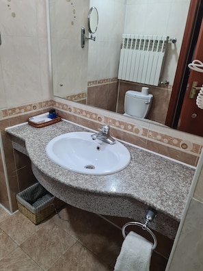 A bathroom with a granite countertop sink, a mirror, a toilet, and a towel rack. - Asia Grand Hotel (Dushanbe)