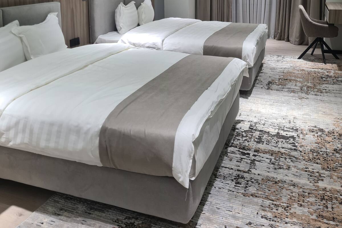 Hotellihuone, jossa on kaksi sänkyä, työpöytä, tuoli ja suuri ikkuna, jossa on verhot.