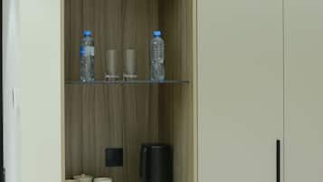 A cabinet with a plant, water bottles, glasses, a coffee maker, and cups.