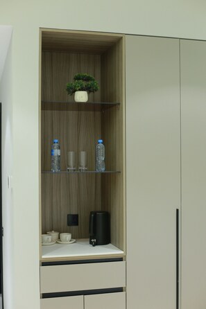 A cabinet with a plant, water bottles, glasses, a coffee maker, and cups. - Asia Grand Hotel (Dushanbe)