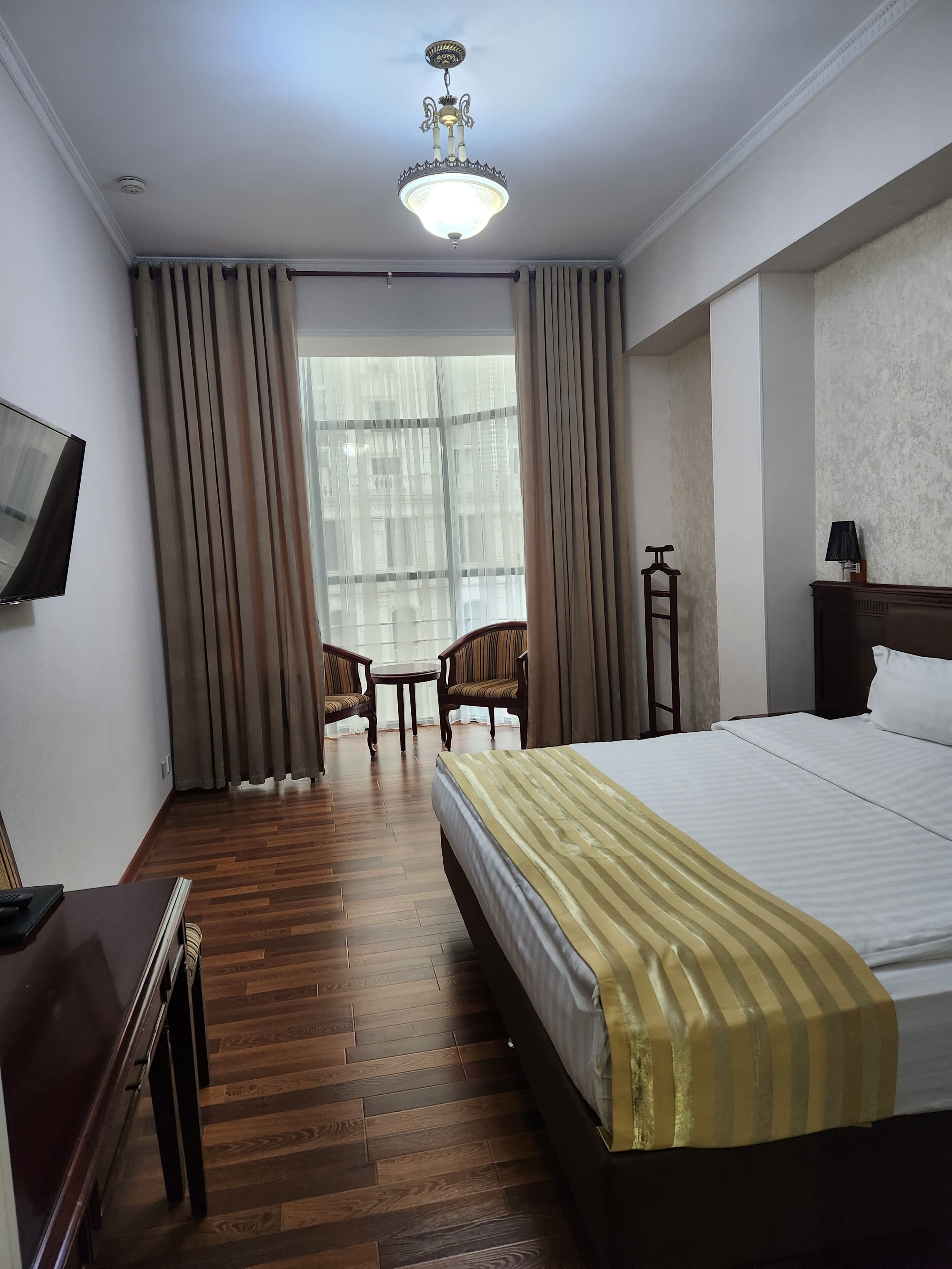 Een hotelkamer met een bed, een bureau, een stoel, een televisie en een raam met gordijnen.