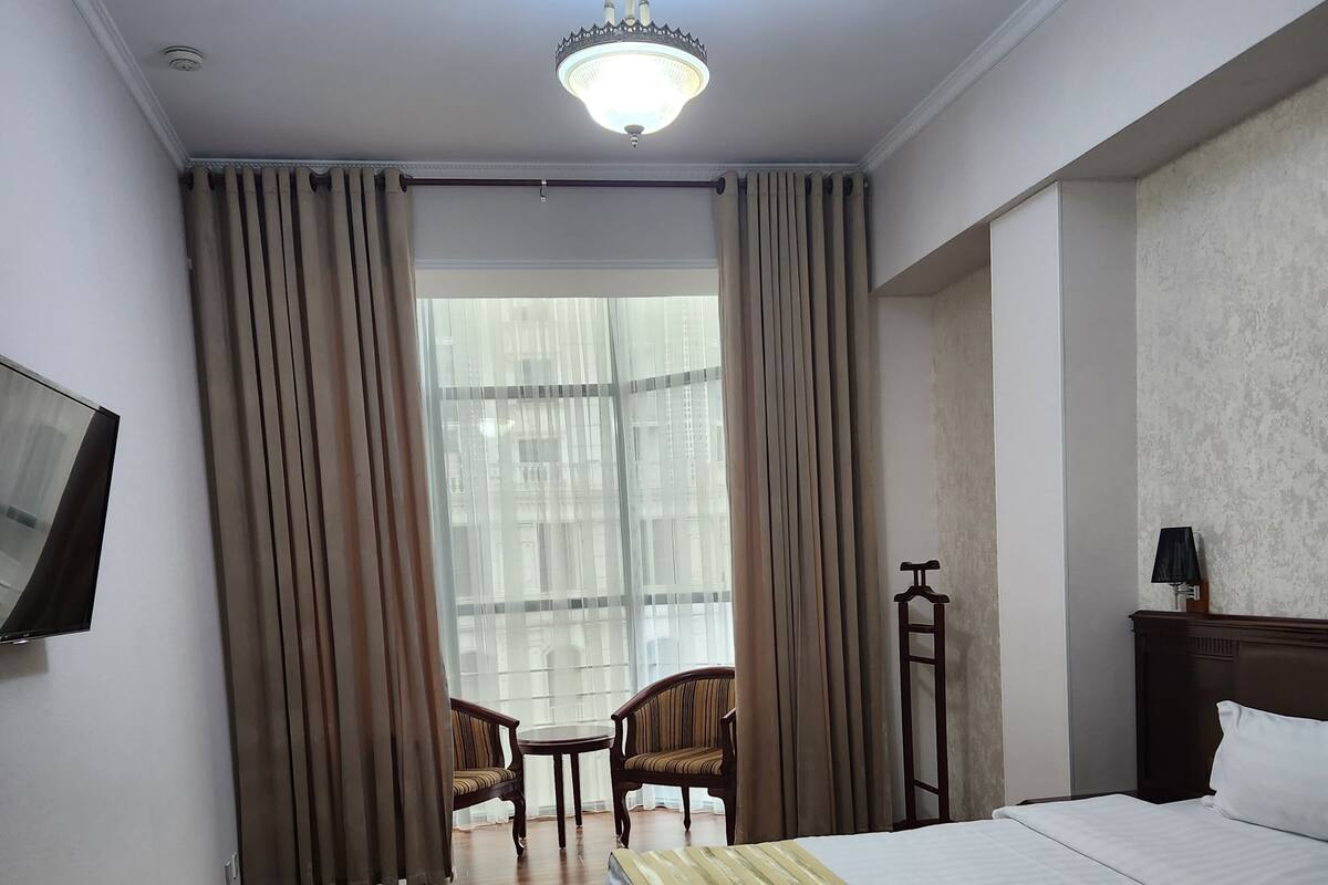 Hotellihuone, jossa on sänky, työpöytä, tuoli, televisio ja ikkuna, jossa on verhot.