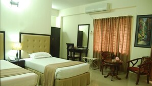 A hotel room with two beds, a desk, a chair, an air conditioner, and a painting on the wall.