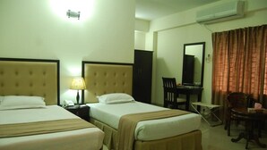 A hotel room with two beds, a desk, a chair, and an air conditioning unit.