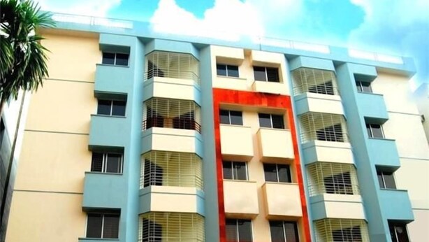 A multi-story building with a central red section, likely a lobby or atrium, flanked by beige and blue sections, with balconies on each floor.
