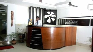 A reception desk with a man standing behind it, a logo on the wall, and a potted plant to the left.