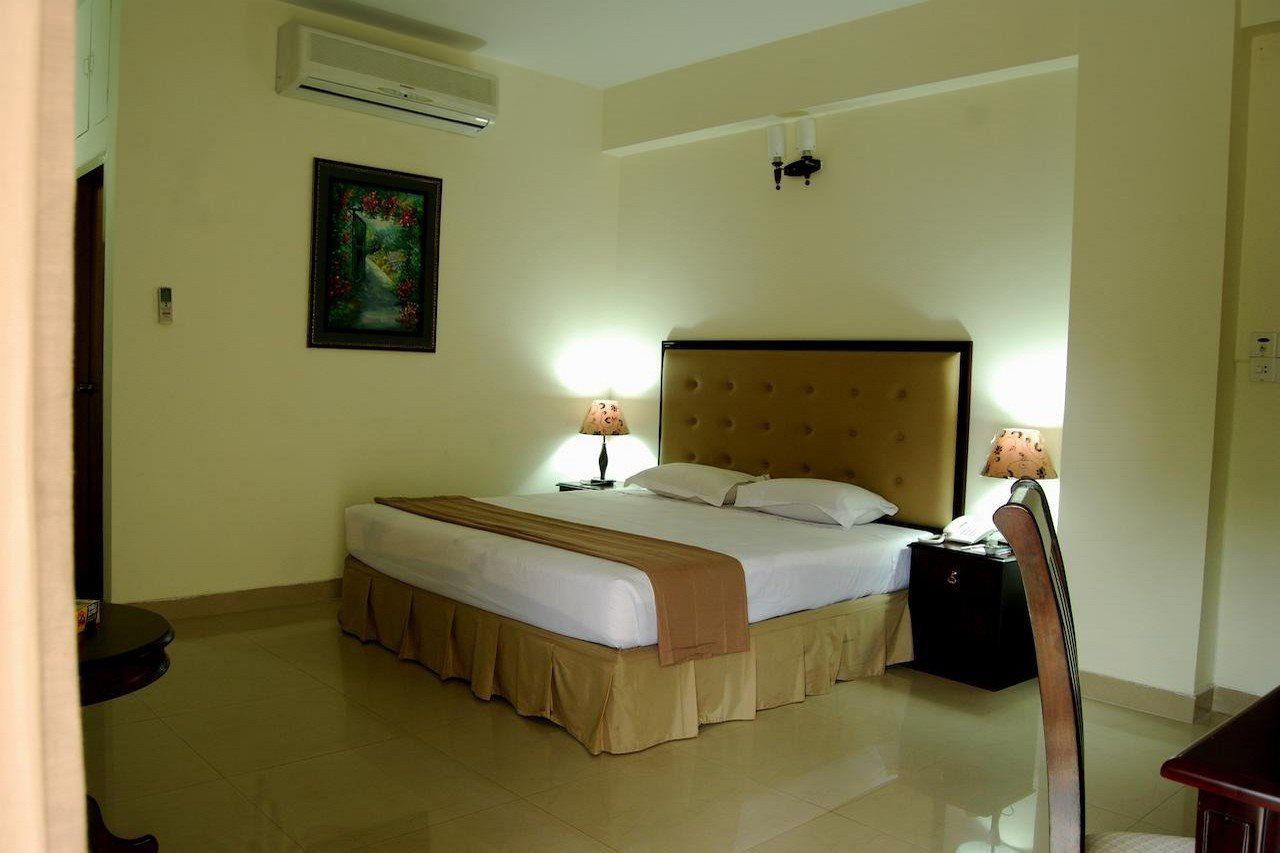 A hotel room with a bed, bedside lamps, a nightstand, and a painting on the wall.