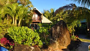 A house with a balcony, surrounded by tropical vegetation and a large rock. - Sokala Villas (Rarotonga)