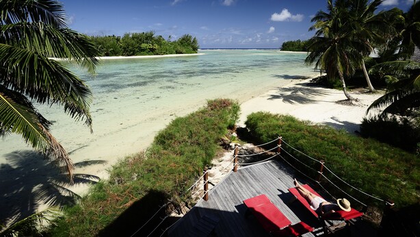 A beach with a wooden deck, lounge chairs, and a clear view of the ocean and distant islands. - Sokala Villas (Rarotonga)