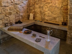 A stone-walled room with a stone bench, a small table with a chessboard, a vase, and various small objects. - Trinity Boutique Hotel (Rhodes)