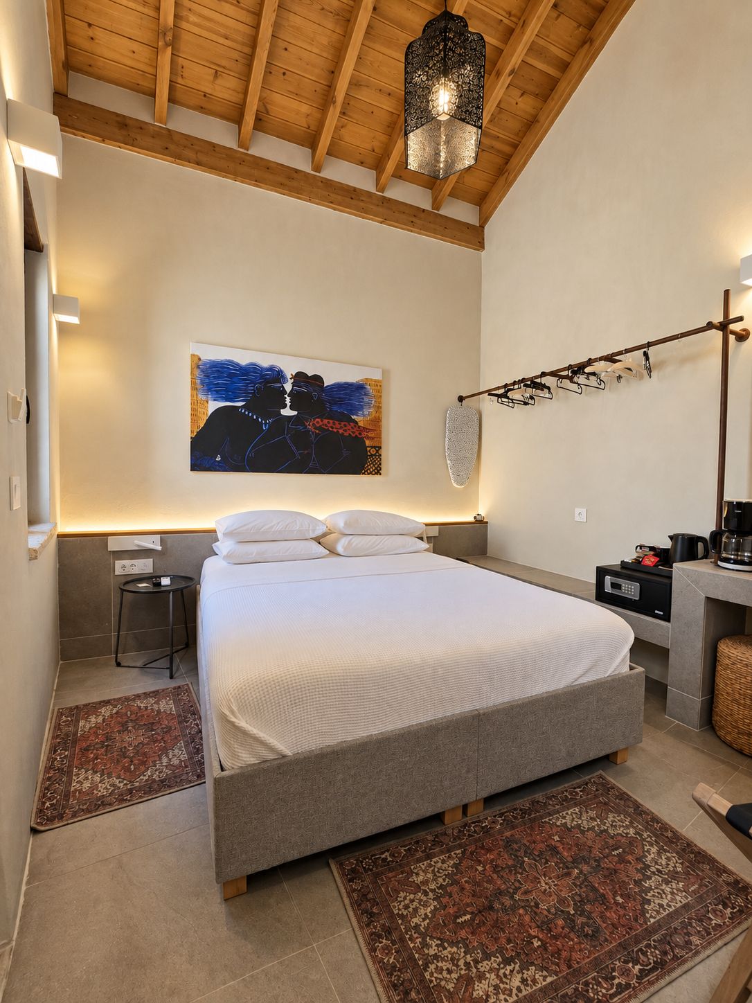 A modern bedroom with a large bed, a hanging light fixture, a painting on the wall, and a side table with a coffee maker.