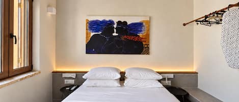 A bedroom with a bed, a painting, a window, and a coat rack.