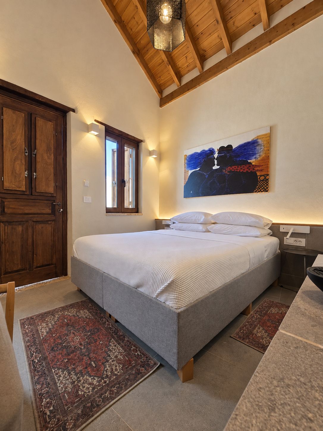 Un dormitorio con una cama grande, vigas de techo de madera, una ventana, un cuadro y una mesita de noche.