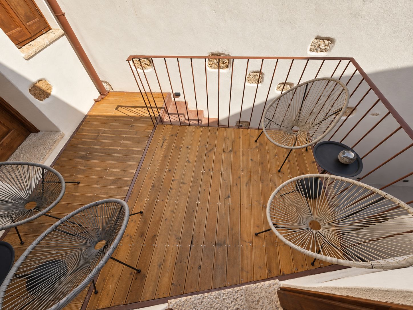 A wooden deck with a metal railing, surrounded by wicker chairs and a small table.
