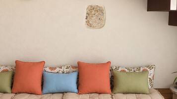 A modern interior with a stone wall, a cushioned bench with colorful cushions, and a staircase with a metal railing.