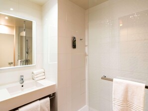 Une salle de bain moderne avec une douche à parois de verre, un lavabo avec un miroir et deux serviettes.
