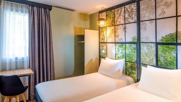 A hotel room with two beds, a desk, a chair, and a view through a window with a tree pattern.
