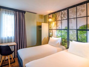 Une chambre d’hôtel avec deux lits, un bureau, une chaise et une fenêtre donnant sur un paysage arboré.