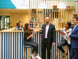 Zona de bar con mostrador y taburetes, estantes con botellas y una pared de listones de madera.