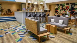 A modern lobby with a wooden reception desk, bar area, seating with sofas and chairs, and a colorful abstract wall. - Ibis Styles Parc des Expositions de Villepinte (Villepinte)
