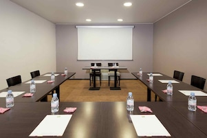 Una sala de conferencias con una pantalla grande, mesas largas, sillas, botellas de agua y papeles.