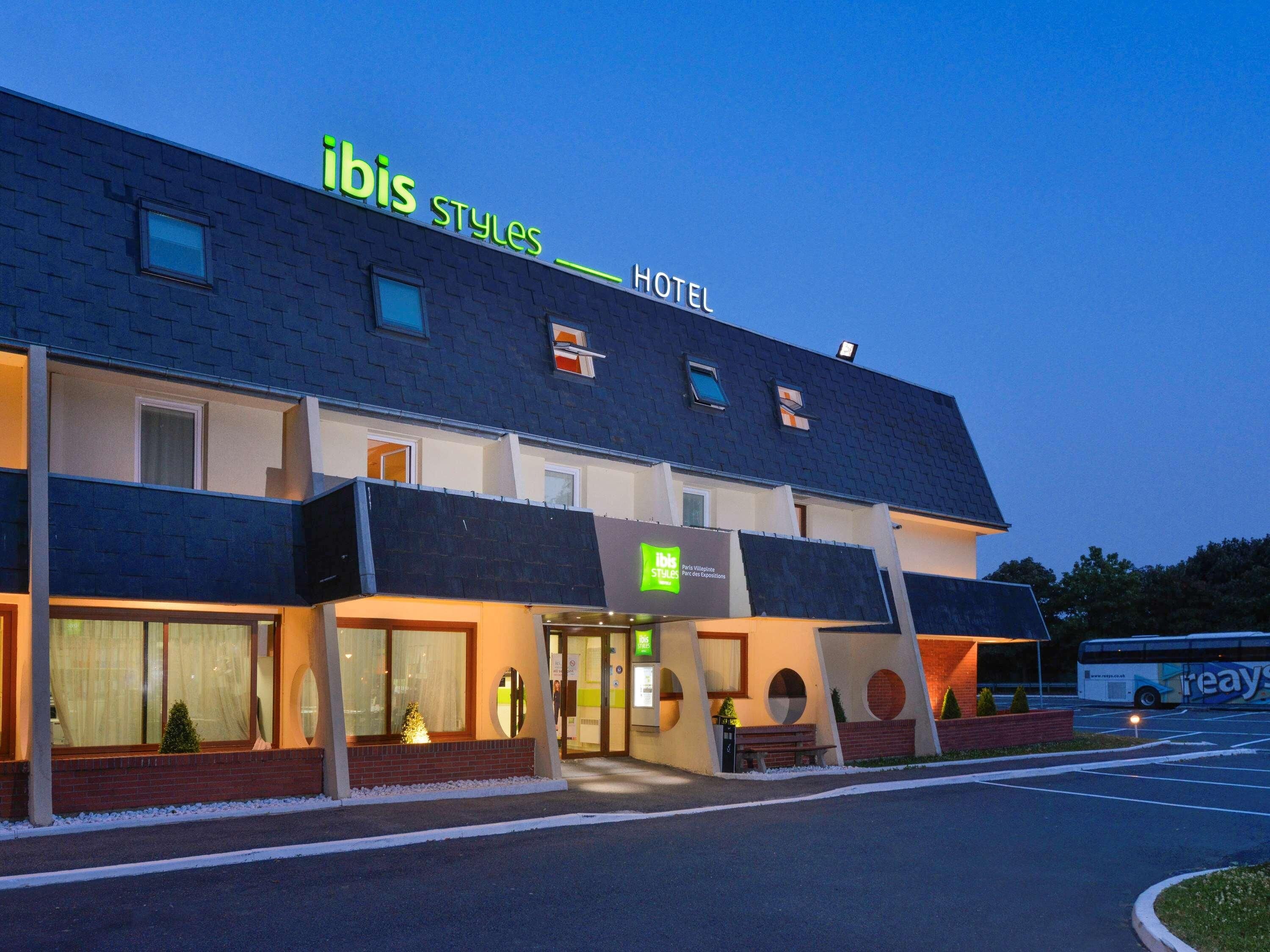 A hotel named "ibis Styles Hotel" with a modern design, large windows, and a parking area.