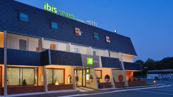 A hotel named "ibis Styles Hotel" with a modern design, large windows, and a parking area.