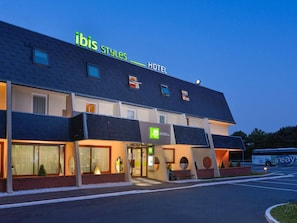 Een hotel genaamd "ibis Styles Hotel" met een modern design, grote ramen en een parkeerplaats.