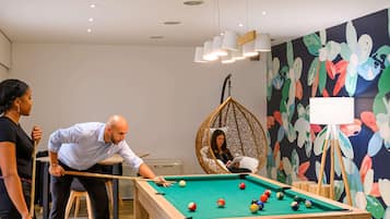 Una mesa de billar en una habitación con un mural colorido, una silla colgante y una pizarra.