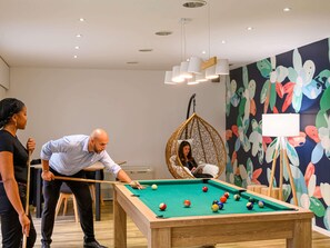 Una mesa de billar en una habitación con un mural colorido, una silla colgante y una pizarra.