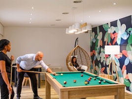 Una mesa de billar en una habitación con un mural colorido, una silla colgante y una pizarra.