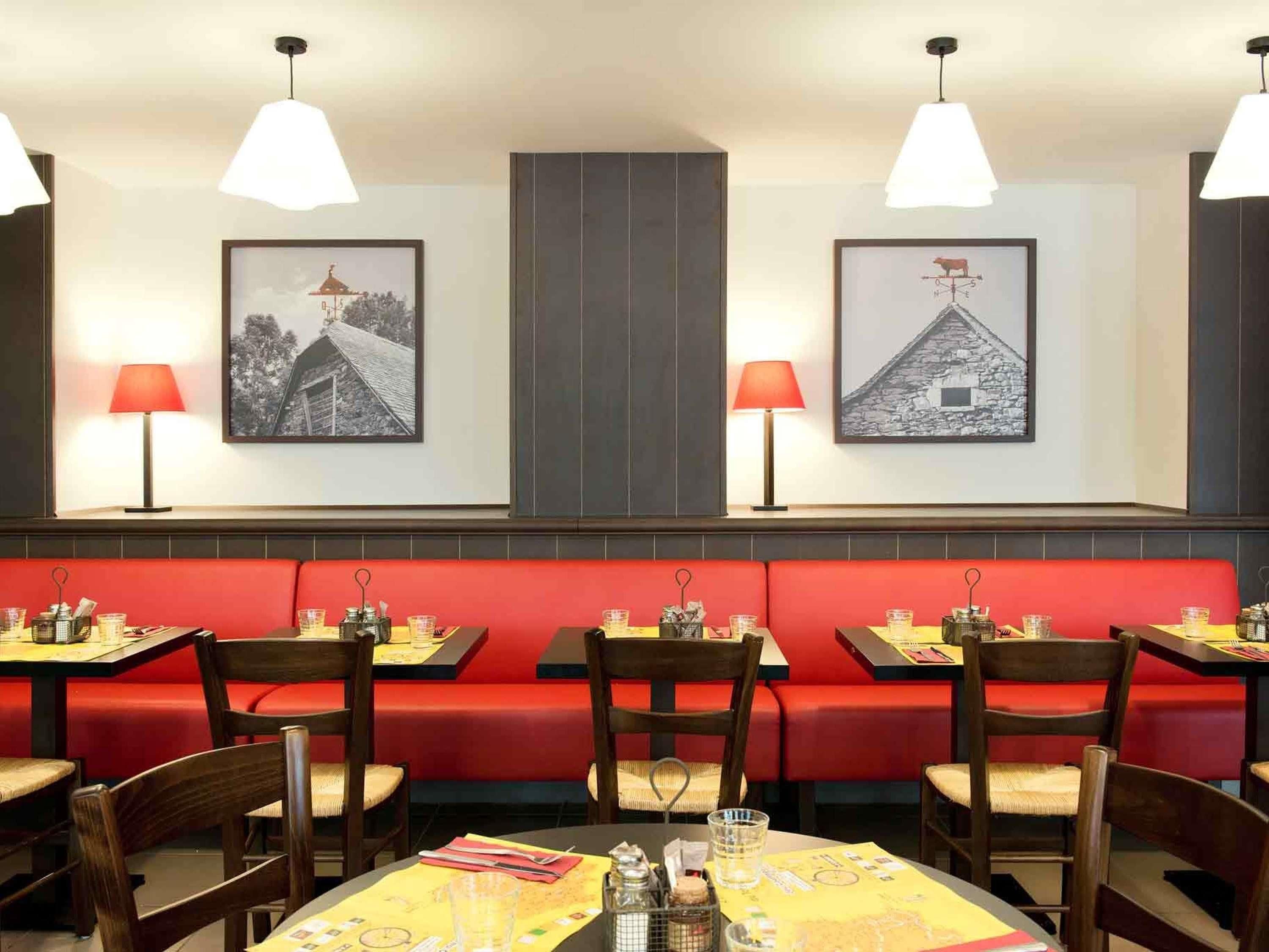 A restaurant with red booths, wooden tables, and pendant lighting.