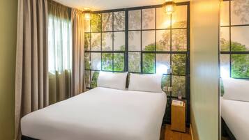 A hotel room with a large bed, two bedside tables, a window with a view of trees, and two wall-mounted lamps.