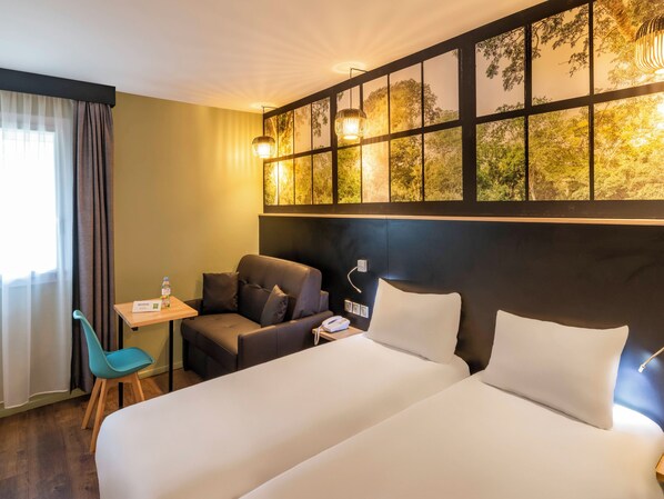 A hotel room with a bed, a desk, a chair, and a view of trees through a window.