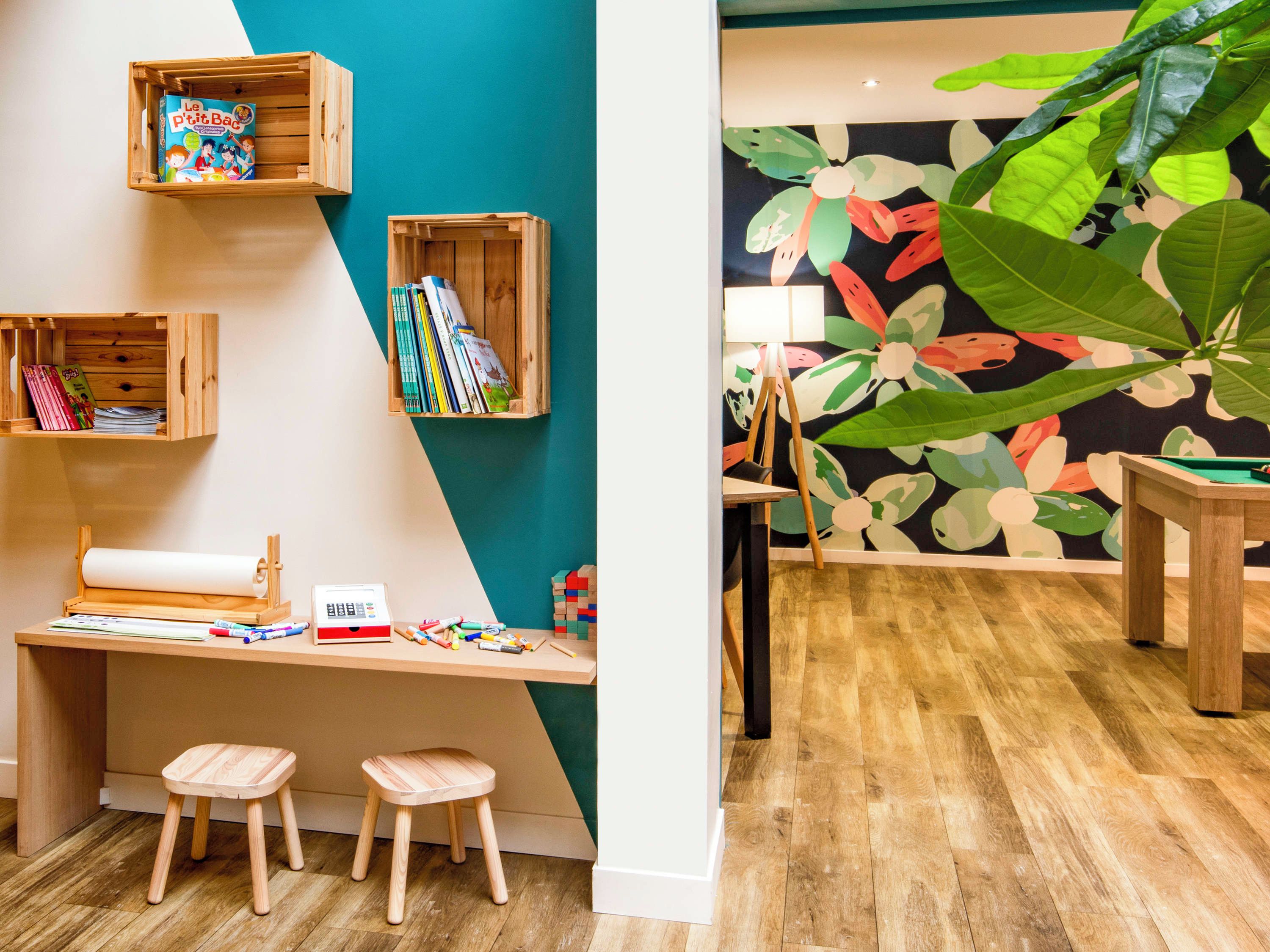 A room with a wooden desk, stools, and shelves with books and toys.
