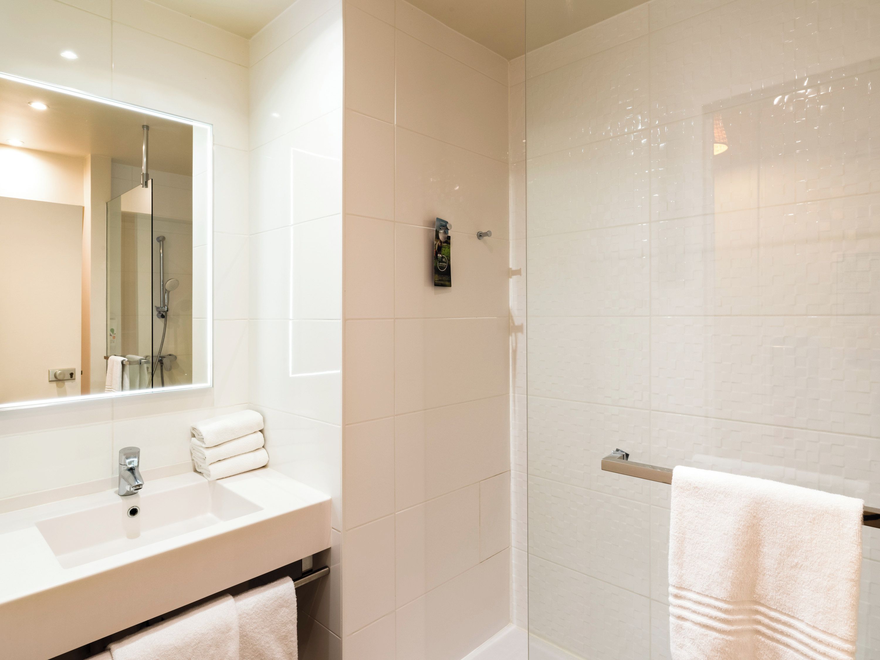 Une salle de bain moderne avec une douche à parois de verre, un grand miroir et un lavabo blanc doté d’un porte-serviettes.