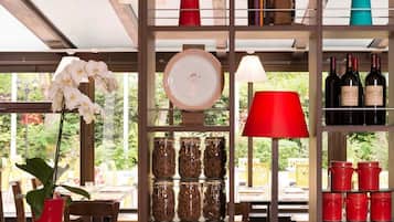 Un espace intérieur bien éclairé, comprenant un coin repas, une étagère remplie de livres, une lampe rouge et une collection de bouteilles de vin.