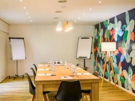 Una sala de conferencias con una mesa de madera, sillas, una pizarra y un mural abstracto y colorido en la pared.