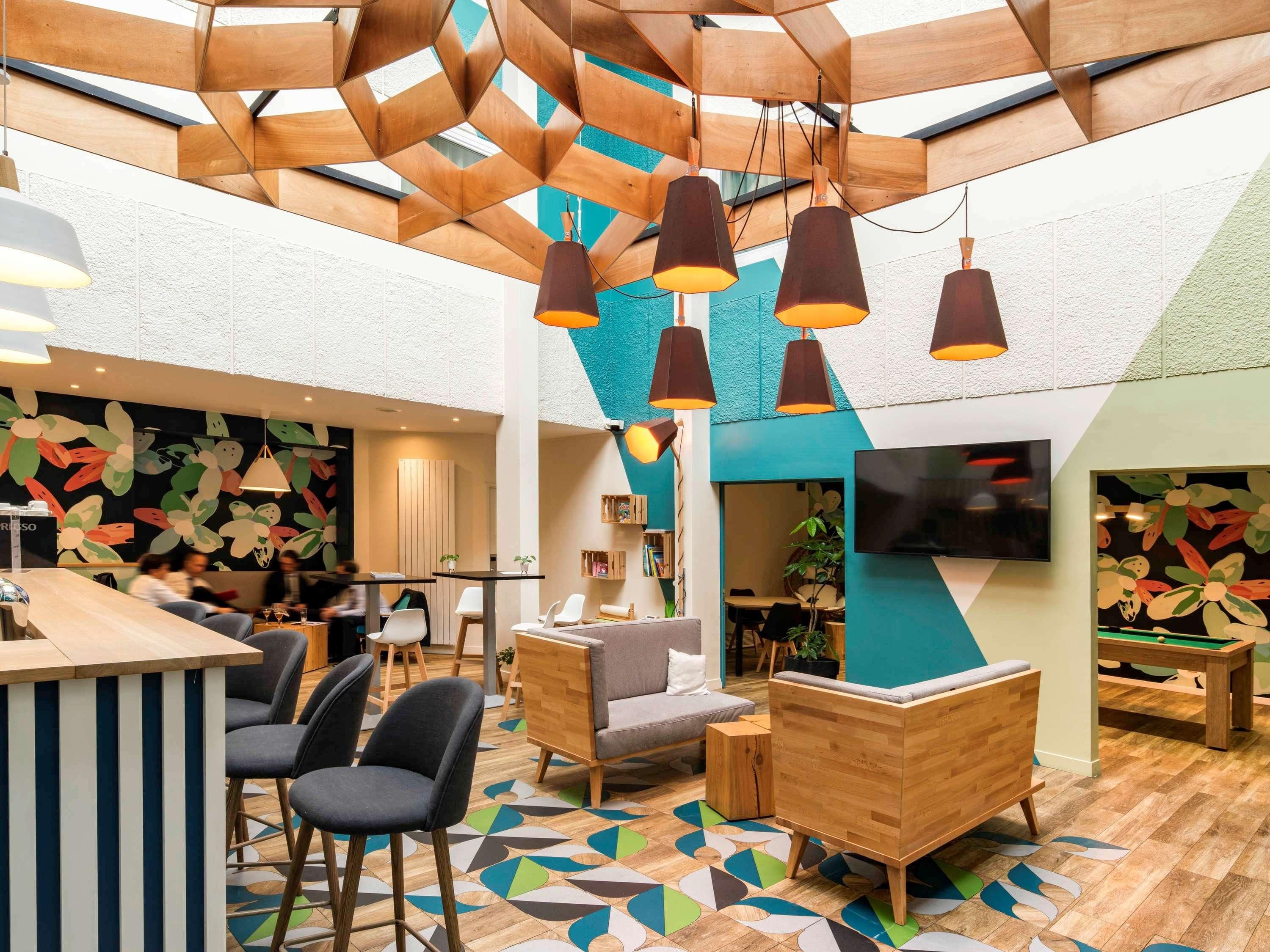 A modern lounge area with a wooden ceiling, geometric wall art, and a pool table.