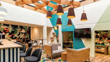 A modern lounge area with a wooden ceiling, geometric wall art, and a pool table.