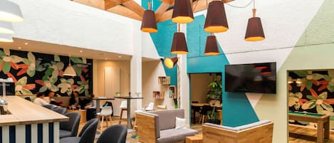 Een moderne lounge met een houten plafond, geometrische wandkunst en een pooltafel.